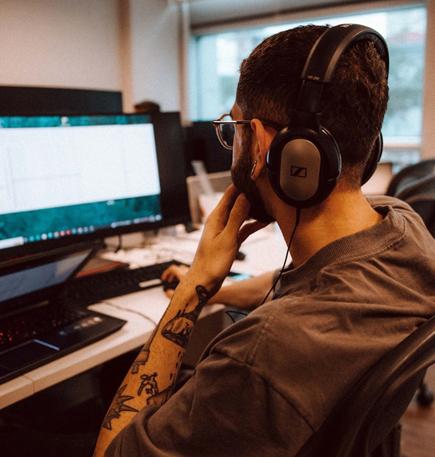 Guy with tattoos on arm is working at a desk Totally digital marketing agency NZ he is wearing headphones