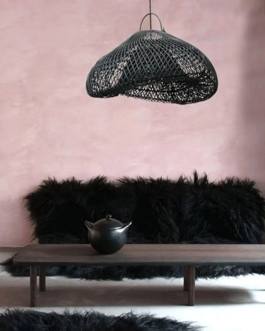 Subtle rose coloured clay wall, fluffy seat, low coffee table, in bowls on table in with oversized, ebony organic shaped cane lampshade, for client Shopify Marketing